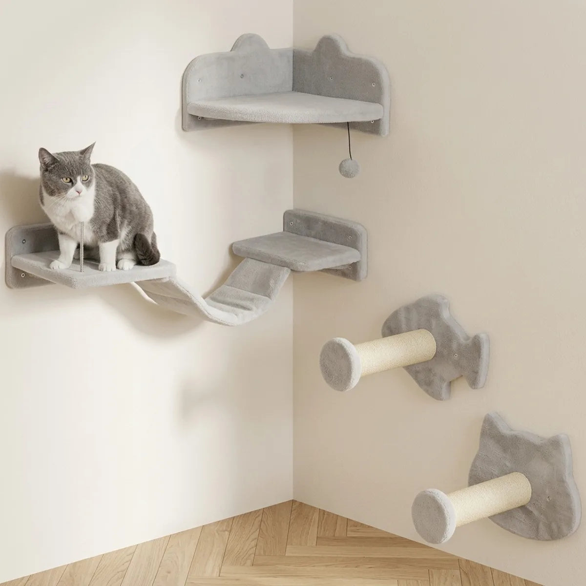 Arbre à chat mural gris clair en angle avec niche suspendue, plateformes, griffoirs sisal et jouet, chat assis sur un perchoir.